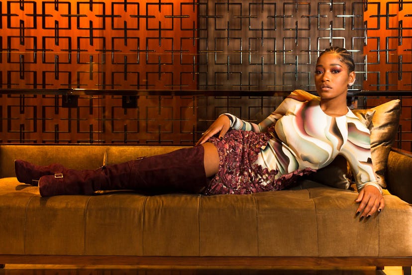 Keke Palmer with tightly braided hair and in a pink shirt lying sideways on a couch 