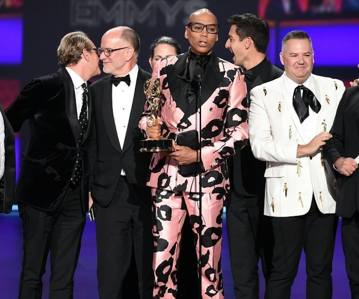 RuPaul on stage at the Emmys accepting an award in a shiny pink suit with black flowers on it