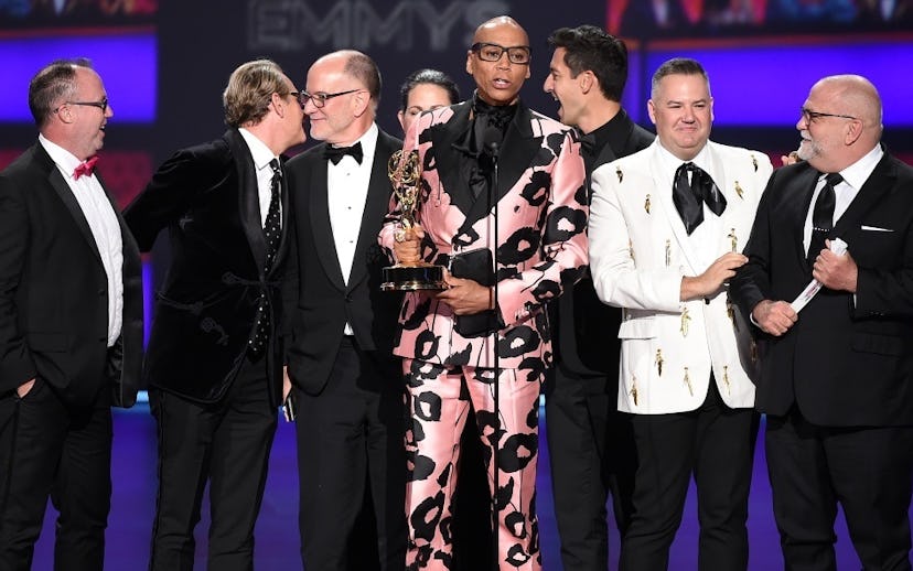 RuPaul on stage at the Emmys accepting an award in a shiny pink suit with black flowers on it