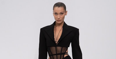Bella Hadid with minimal make-up, ponytail and a sheer corset and lined tights under her suit