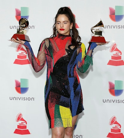 Rosalia posing in a colorful dress while holding two awards in her hands