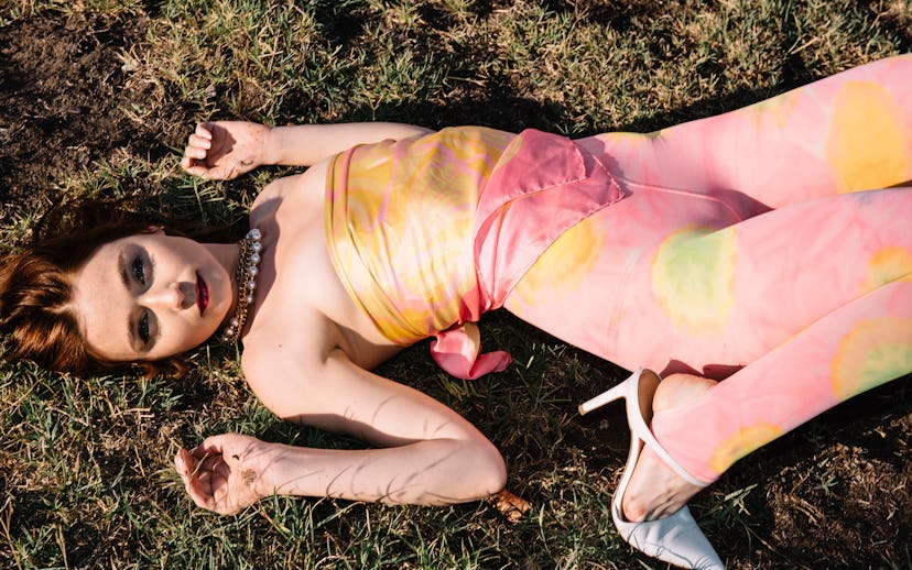 Jessica Barden lying on the grass in a peach-yellow silk wrap-tie top, peach-yellow tulle leggings, ...