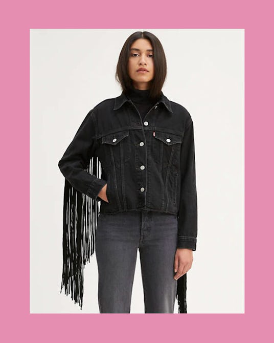 A brunette woman posing in a black fringe trucker jacket by Levi's