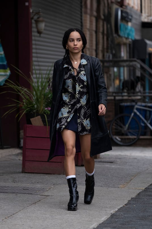 Zoe Kravitz in a black trench coat with black leather boots and a patterned shirt walking down the s...