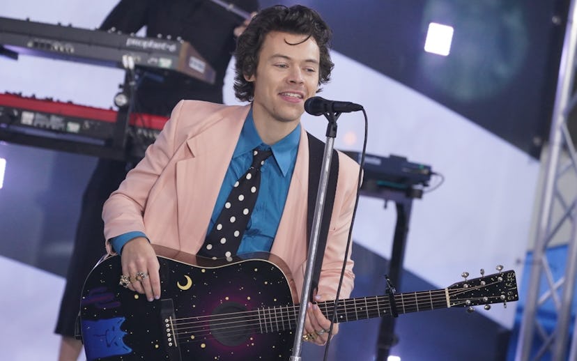 Harry Styles singing and playing guitar in a blue shirt, black tie with white polka dots and a pink ...