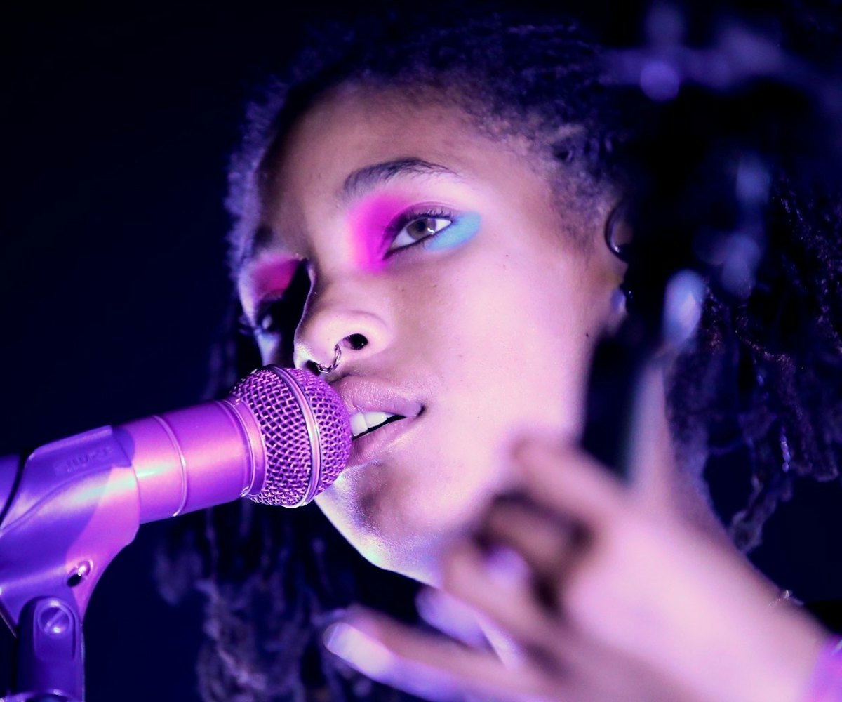 Willow Smith with neon makeup and bathed in purple light singing into a microphone 