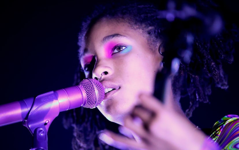 Willow Smith with neon makeup and bathed in purple light singing into a microphone