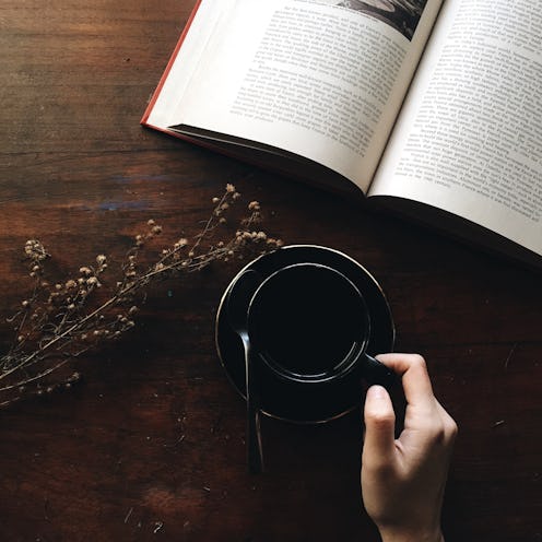 A woman holding a cup of coffee with an open book on a table in front of her