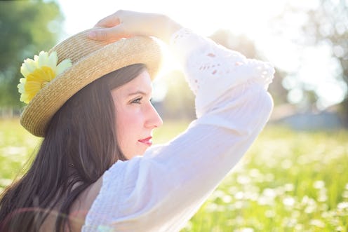 Woman in a straw hat with a flower in it standing in a field on a sunny day