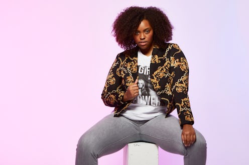 A young curly and black-haired lady posing in a black jacket with golden drawings