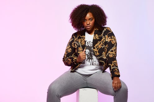 A young curly and black-haired lady posing in a black jacket with golden drawings