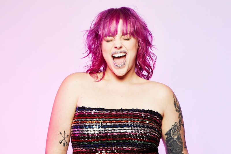 A woman with fuchsia pink hair and a paillette tank top smiling