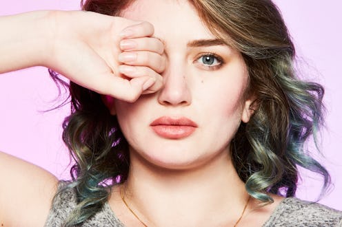 A brunette woman with her right fist covering her right eye