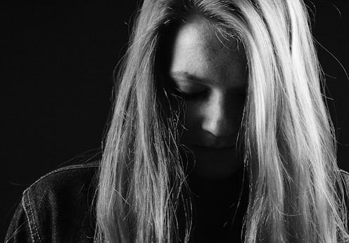 A blonde woman struggling with addiction standing in the dark.