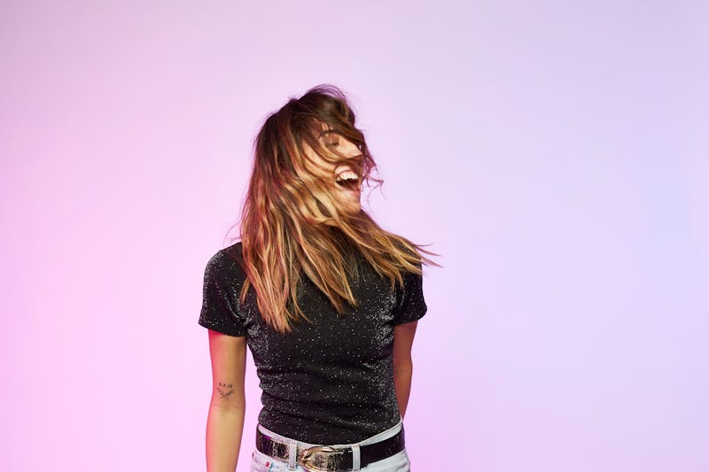 A single woman wearing a black t-shirt and jeans smiling while her hair is covering her face