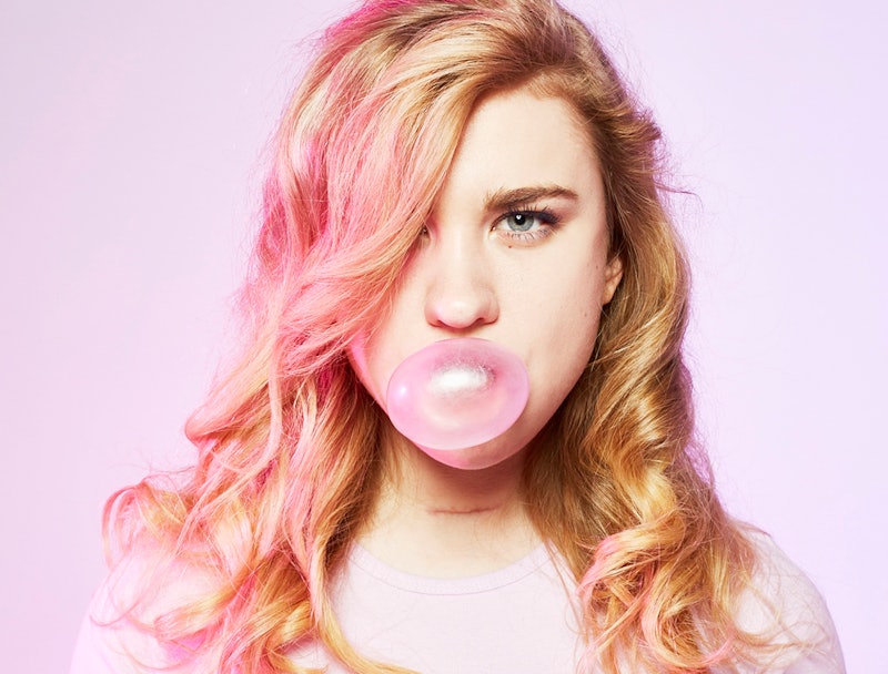 Blonde woman wearing a pink T-shirt while blowing a pink bubble gum