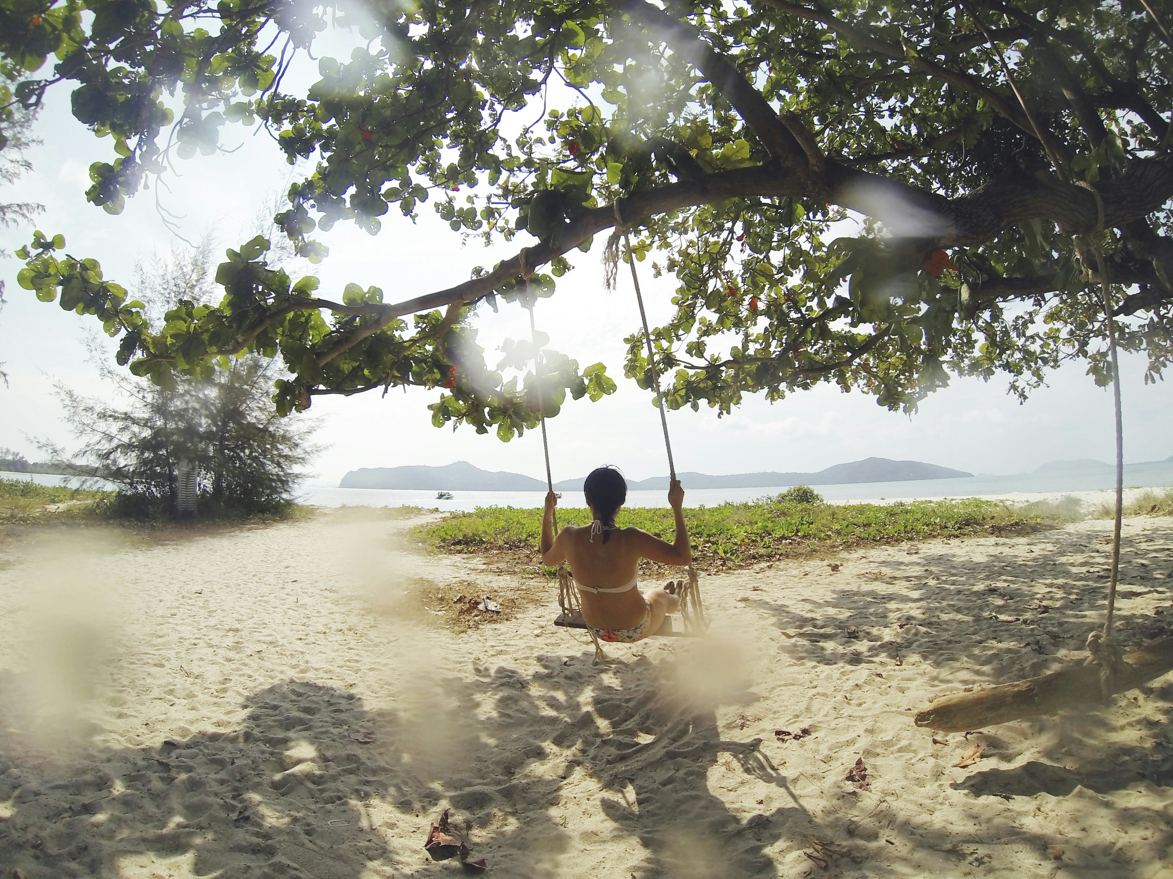 A woman wearing a bikini sitting on a swing set on a tree near the beach