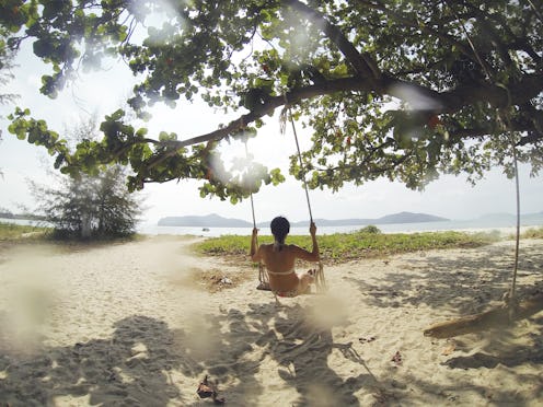 A woman wearing a bikini sitting on a swing set on a tree near the beach