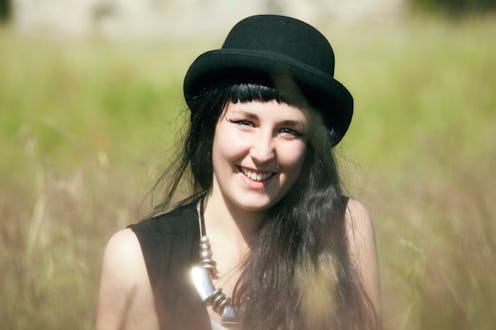 A woman sitting in tall grass with a black bowler hat smiling after running