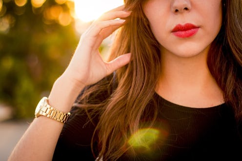 A brunette woman leaning her hand near her face wearing a black top and golden watch