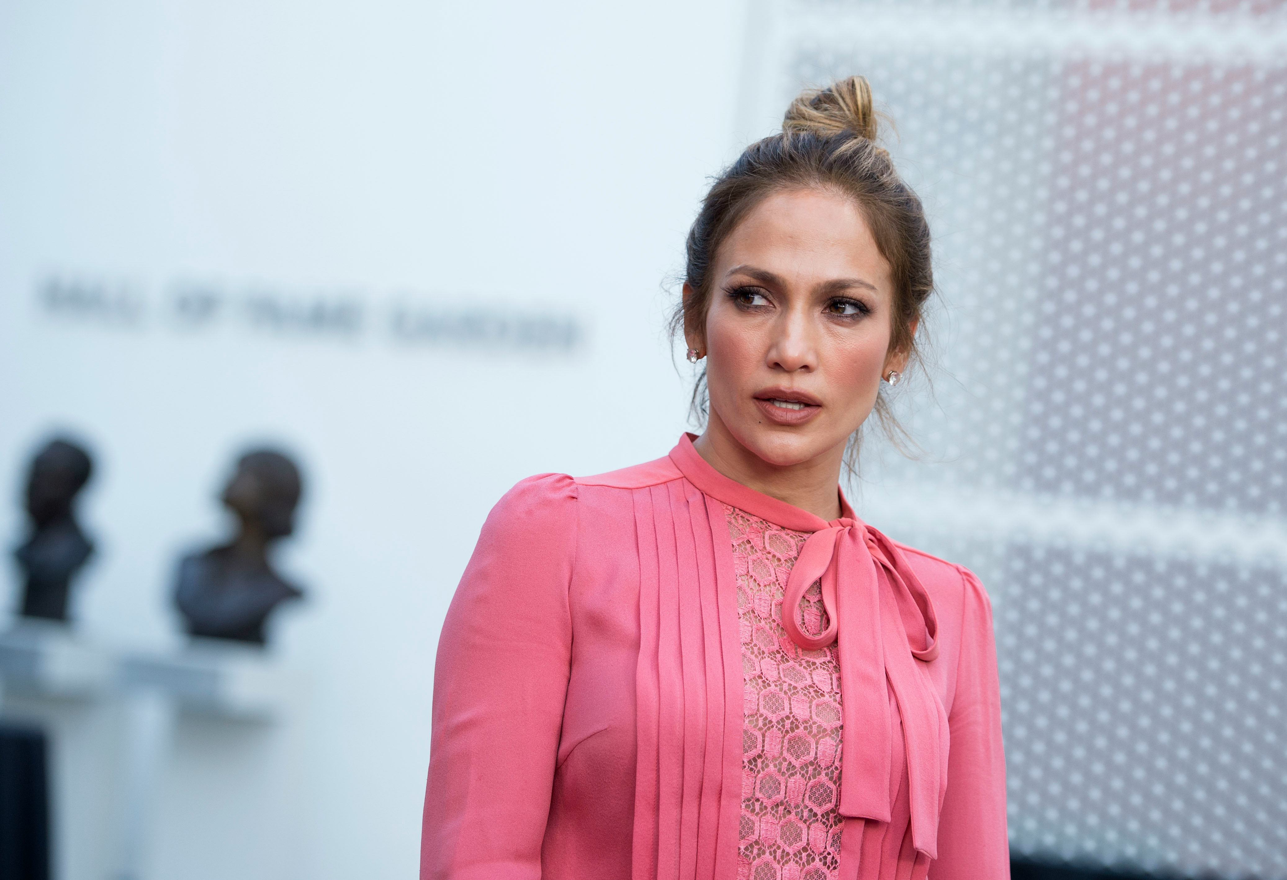 Jennifer Lopez with her hair in a bun wearing a pink outfit and looking off to the side