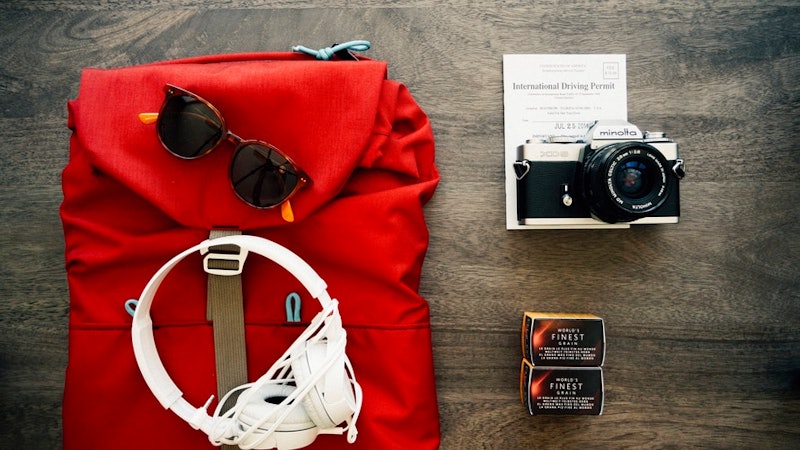 Red backpack, sunglasses, headphones, camera and a notebook