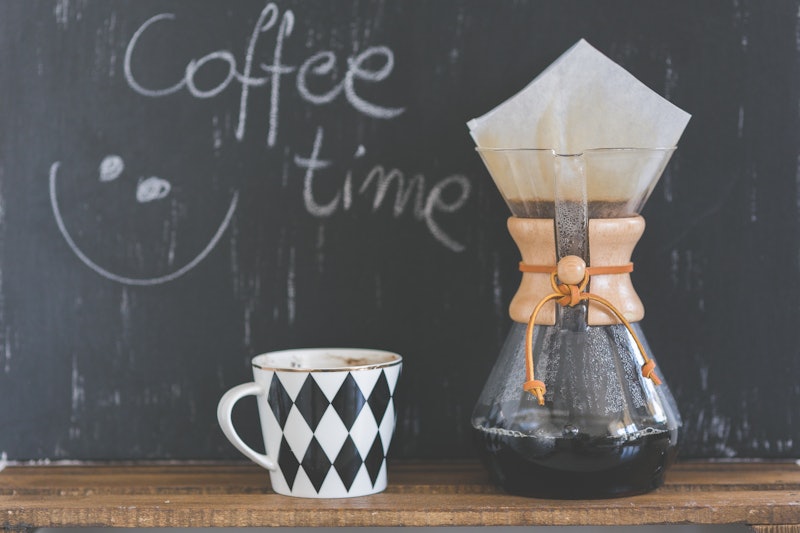 "Coffee time" sign written in chalk on a blackboard with a cup and and glass jar of coffee beside it...