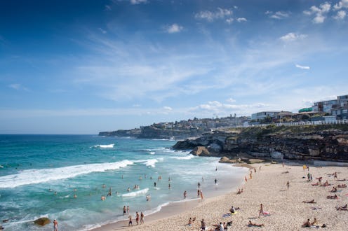 People lying on a sandy beach, and some of them swimming while the waves are coming closer to the ro...