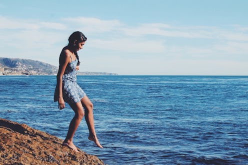 A woman in a blue swimsuit dipping her foot in the ocean on a sunny day