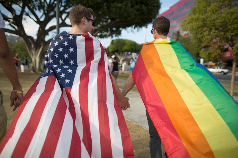 Two gay men, holding hands and draping flags of the LGBTQ community and the USA national flag over t...