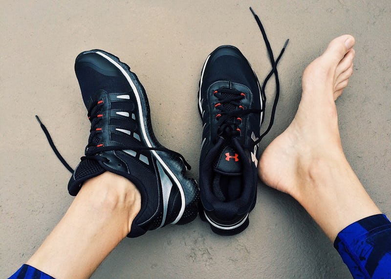 A person sitting on a floor with one of his sneakers off because of running pains