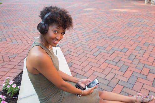 A woman sitting on a bench wearing headphones and holding her phone while smiling