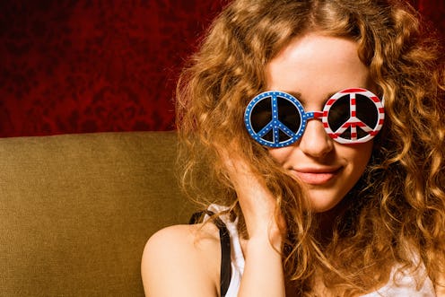 A girl with red curly hair wearing red-and-blue sunglasses shaped like a peace sign for the Fourth o...
