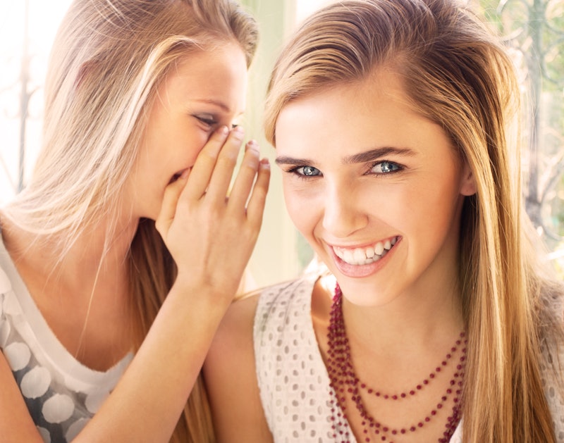 A blonde woman whispering something to her friend while she is giggling.