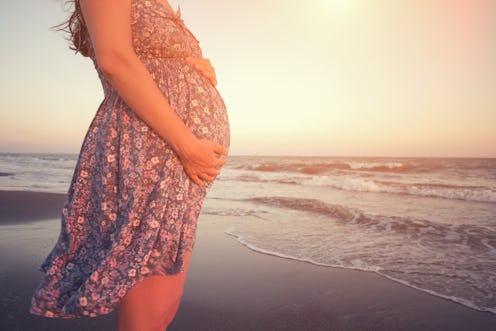 A pregnant woman in a floral dress at the beach who has PCOS