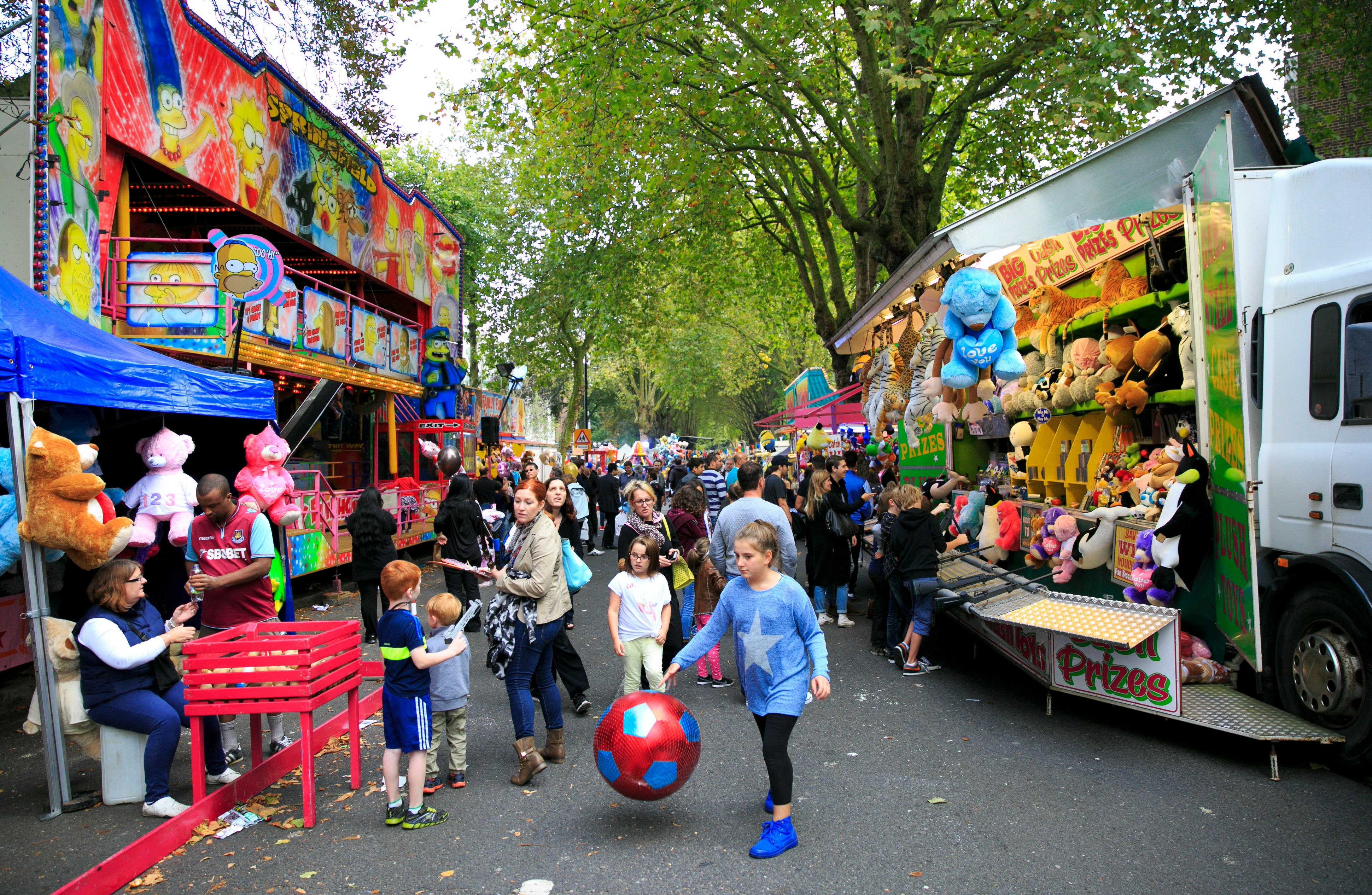 A fair located on the street, with various games, prizes, snacks, treats and people going by