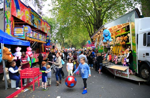 A fair located on the street, with various games, prizes, snacks, treats and people going by
