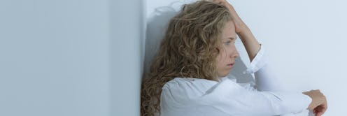 A curly-haired blonde woman diagnosed with Schizophrenia, wearing a white shirt while leaning on whi...