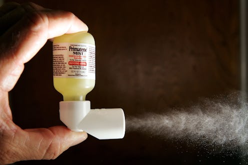 A hand pressing an inhaler, which sprays forward