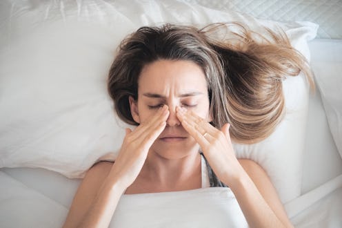 A woman lying in a bed, and holding her hands on her nose because she is sick