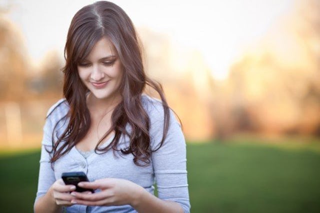 A brunette woman smiling and looking at her phone, making online mom friends