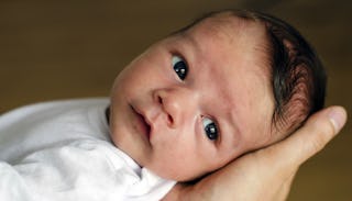 A newborn leaned to someone's hand dressed in a white shirt for brunch.