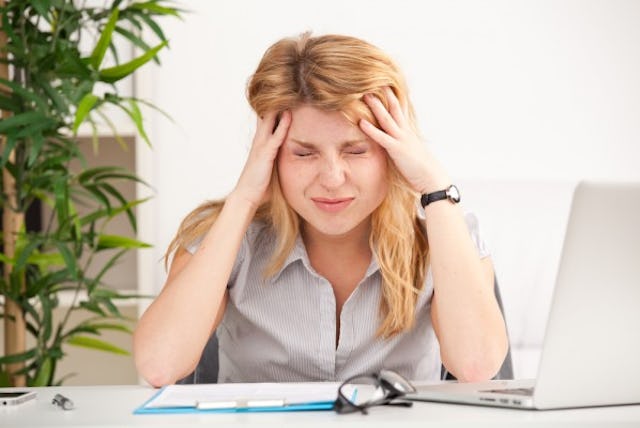 A woman holding her aching head in the office