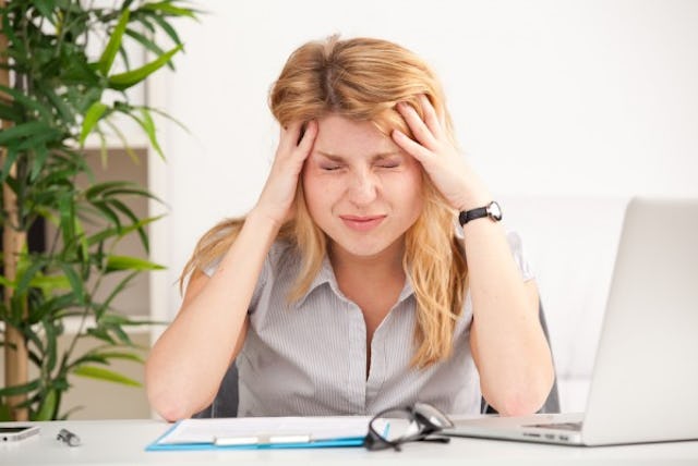 A woman holding her aching head in the office 