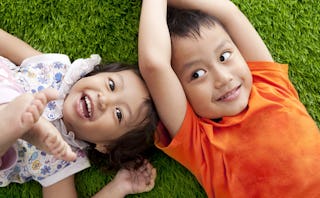 Two foster siblings laying on a grassy surface and smiling