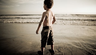 An autistic child standing on the beach looking at the sea in black and white