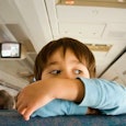 A boy leaning on a seat with his arms crossed on his chin in an airplane