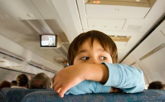 A boy leaning on a seat with his arms crossed on his chin in an airplane