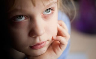 A brown-haired child leaning their head on their hand while looking upwards 