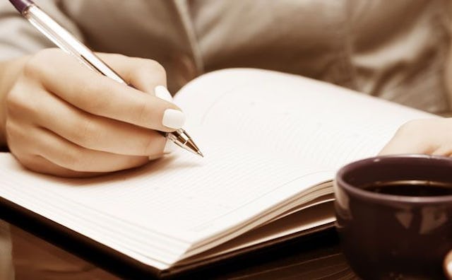 A close-up of a woman writing a letter to her younger self in a notebook